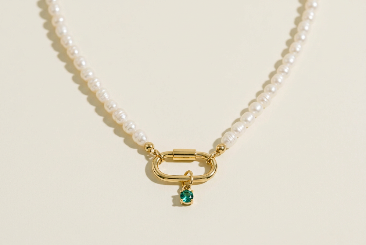Freshwater pearl necklace with gold carabiner clasp and birthstone charm on a cream background